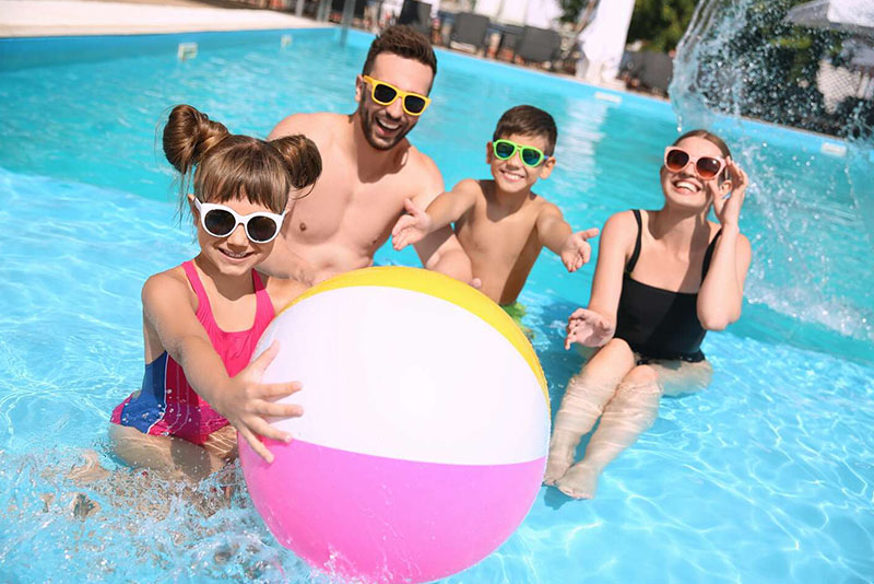 Family playing with a beach ball in the pool is ready for new family swimming pool games.