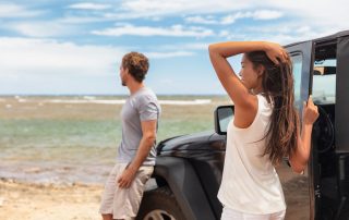 Couple on a road trip travel in Hawaii driving car on beach